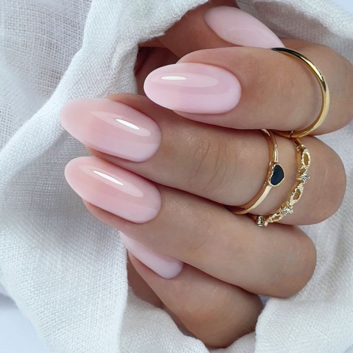 Milky roze amandelnagels met gouden ringen op wit linnen