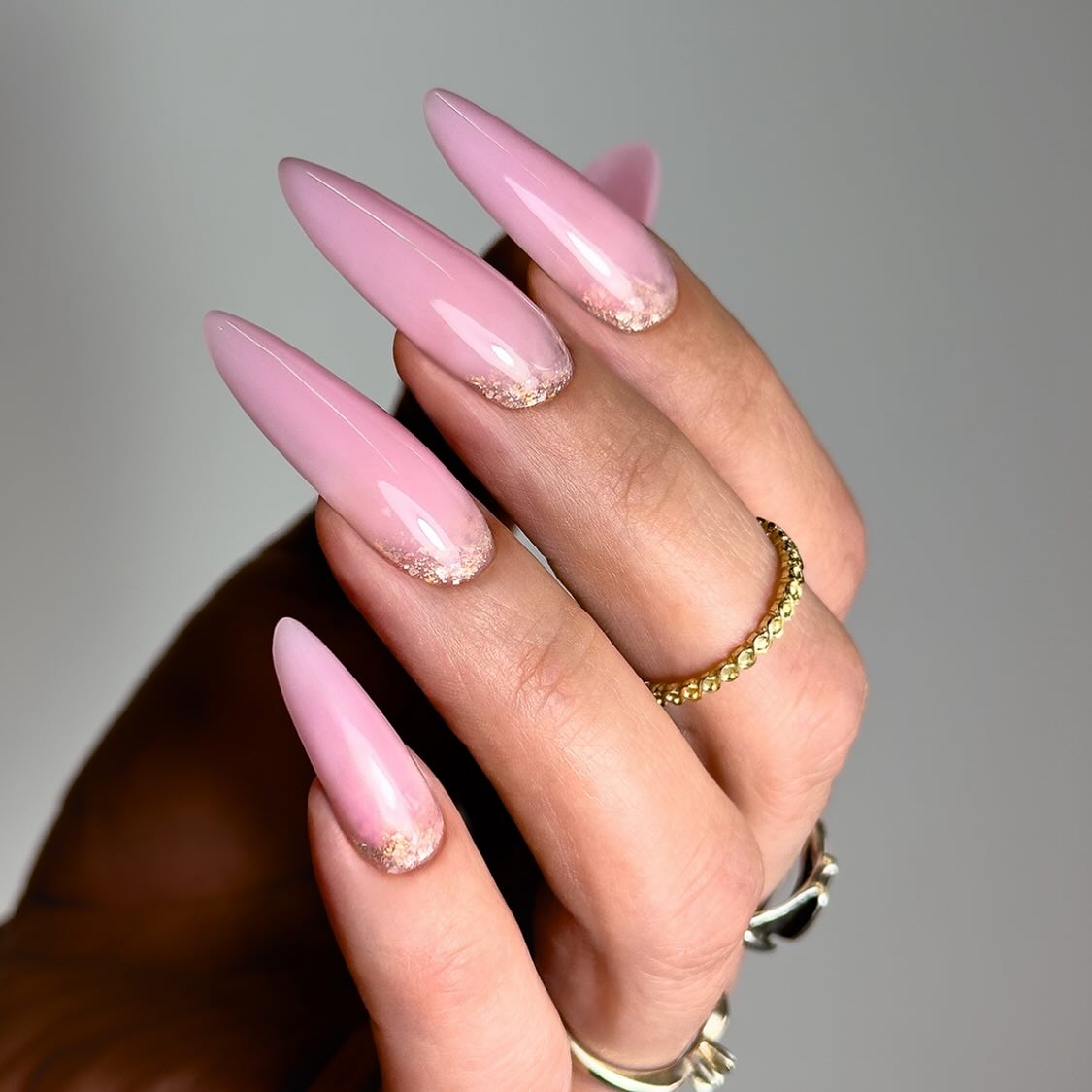 Lange roze amandelnagels met gouden glitter op de punt